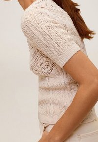 Pletený svetr s krátkým rukávem v světlé krémové barvě, s texturovaným krajkovým vzorem, žebrovaným výstřihem a manžetami. Lehký, přiléhavý střih.