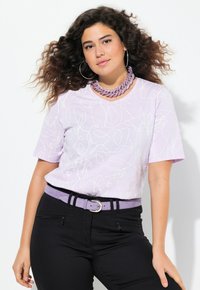 Camiseta de manga corta lila con patrones de líneas blancas abstractas, combinada con pantalones negros y un cinturón lila a juego. Presenta grandes pendientes de aro.