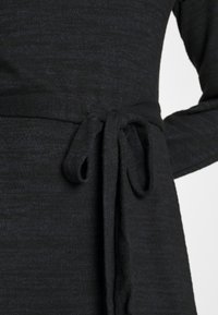 Czarny, teksturowany materiał odzieżowy z przewiązanym w talii paskiem, z długimi rękawami i miękką, lekko ułożoną sylwetką.