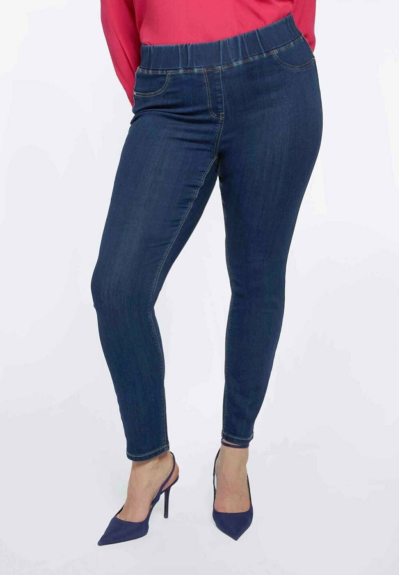 Tummansiniset farkkuleggingsit, joissa on joustava vyötärö, slim fit -malli ja kontrastiväriset tikkaukset. Yhdistetty tummansinisiin korkokenkiin.