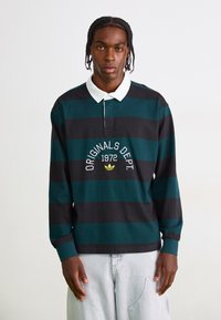 Camisa polo de manga longa em verde escuro com riscas pretas, apresentando um colarinho branco e um gráfico frontal com texto e logótipo. Material em algodão.