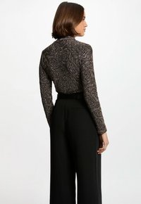 Pantaloni neri a gamba larga abbinati a una maglietta aderente a maniche lunghe con un motivo floreale metallico in tonalità di nero e oro.