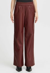Bordeaux faux leren wijde pijpenbroek met een gestructureerde afwerking, voorzien van een elastische tailleband en zijzakken, gestyled met enkellaarsjes.