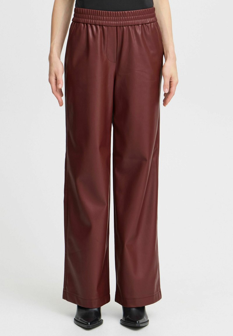 Bordeaux faux leren wijde pijpenbroek met een gestructureerde afwerking, voorzien van een elastische tailleband en zijzakken, gestyled met enkellaarsjes.