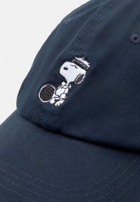 Námořnická modrá baseballová čepice vyrobená z bavlny, s vyšitým designem Snoopyho držícího tenisovou raketu vpředu. Texturovaná tkanina, zaoblený kšilt.