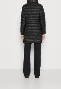 Chaqueta de plumas negra con cinturilla ajustada, acolchado horizontal y cuello alto. Acompañada de pantalones anchos negros.