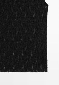 Zwarte kanten top met een gestructureerd bloemenpatroon, mouwloos ontwerp en een onafgewerkte zoom. De stof is lichtgewicht en halfdoorzichtig.