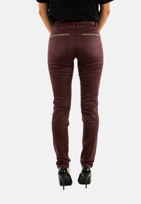Jeans skinny burdeos hechos de material elástico, con bolsillos traseros con cremallera y una textura suave, combinados con tacones altos negros.
