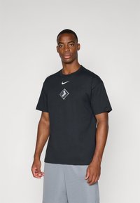 Crna pamučna majica s okruglim izrezom, kratkim rukavima i bijelim Nike logom iznad grafike u obliku dijamanta na prsima.