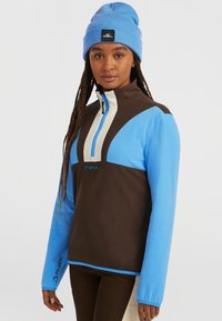 Halve rits fleece pullover in bruin en blauw, met een beige accent, lange mouwen en een Polartec-logo op de mouw.