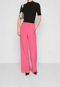 Jasnoróżowe szerokie spodnie z przednimi kieszeniami i subtelnym rozcięciem u dołu, w połączeniu z dopasowanym czarnym topem z krótkim rękawem i ciemnymi szpilkami.