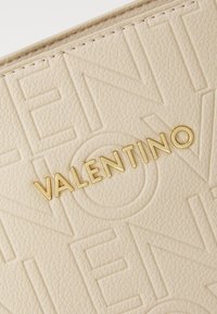Beige textured leather with embossed "VALENTINO" logo in gold. Features subtle geometric patterns and stitched edges for durability.