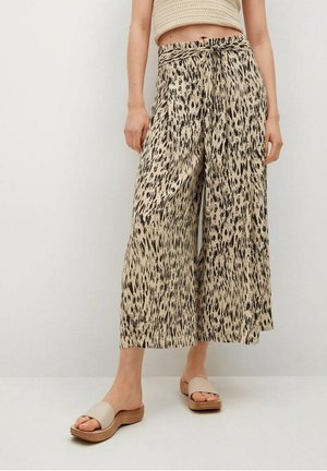 Beige wide-leg trousers with a black spotted pattern, featuring a knotted waistband, and paired with neutral slide sandals.