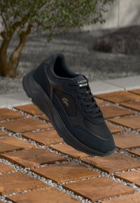 Sneaker nera Lacoste con tomaia in pelle liscia e suede, chiusura con lacci, suola in gomma spessa e dettaglio del logo metallico sul lato.