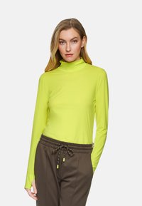Neon yellow long-sleeve turtleneck shirt made of lightweight fabric, paired with brown trousers featuring drawstring and subtle texture.
