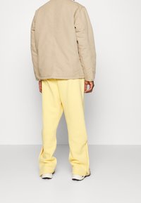 Beige quiltet jakke med rund hals, parret med bløde gule sweatpants med sideslidser, iført hvide og grå sneakers.