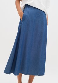 Denim midi-hame syvällä sinisellä värillä, jossa on levenevä muotoilu, sivutaskut ja sileä pinta. Kontrastiväritys helman ympärillä.