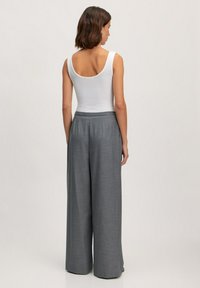 Pantalons larges gris avec un motif texturé, dotés d'une taille haute et de poches latérales, associés à un haut sans manches blanc.
