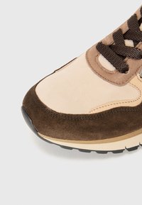 Baskets en daim beige et marron foncé vues de face avec des lacets marron foncé et des coutures détaillées sur un fond clair.