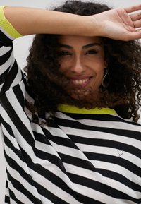 Black and white striped sweater with a bright yellow neckline, featuring a small decorative accent near the bottom. Soft texture, loose fit.