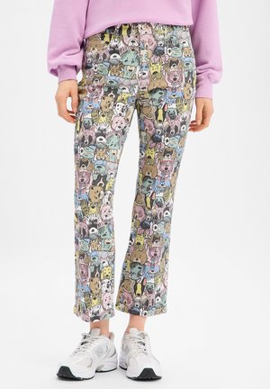 Leggings mit buntem Muster aus Comic-Hundefiguren, getragen zu weißen Sneakers und einem pinkfarbenen Langarmshirt vor weißem Hintergrund.