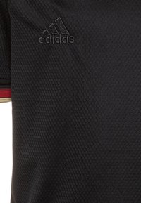 Jersey nero con texture e motivo esagonale, dotato di un piccolo logo Adidas nero e dettagli rossi e dorati sul colletto.