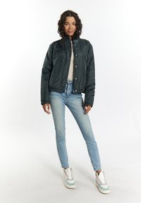 Giacca bomber trapuntata verde scuro con chiusura a bottoni, polsini ed orlo elasticizzati. Abbinata a jeans azzurri e sneakers multicolori.