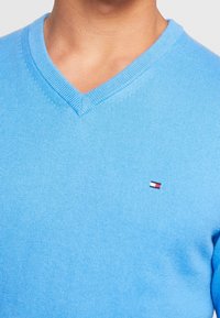 Helles blaues V-Ausschnitt-Pullover aus Strickstoff. Verfügt über ein kleines rot-weiß-blaues Logo auf der linken Brust sowie über einen gerippten Kragen und Saum.