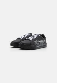 Czarne skórzane sneakersy z białymi sznurówkami, gumową podeszwą i stylizowanym logo "VERSACE JEANS COUTURE" na boku.