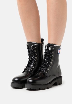 Zwarte leren veterschoenen met bontvoering, robuuste zool en zijrits. Voorzien van een logopatch op de enkel. Soepele textuur en stevig ontwerp.