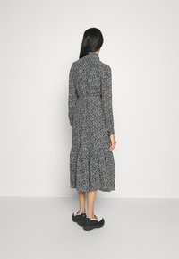 Svart och vit blommig mönstrad midiklänning med långa ärmar, inringad midja och flikad kjol. Kombinerad med tjocka svarta stövletter.