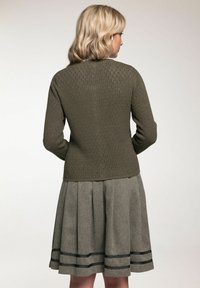 Un pull en tricot vert olive avec un motif texturé et une taille cintrée, associé à une jupe grise à plis et à des rayures noires.