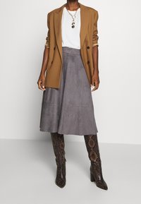 Brun blazer, hvid t-shirt, grå ruskinds midi-nederdel og brune støvler i slangeskind til knæene. Kæden Halskæde fuldender outfittet.