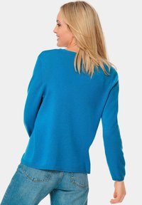 Blau gestrickter Pullover mit langen Ärmeln, rundem Ausschnitt und lässiger Passform. Strukturiertem Stoff und geribbeltem Saumdetail am unteren Ende.