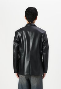 Schwarze Lederblazer mit glatter Textur, taillierter Passform und Reverskragen. Verfügt über sichtbare Nähte und einen etwas längeren Rücken.