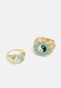 Duas alianças em exibição: uma banda em ouro com um design de yin-yang, e uma aliança em ouro em forma de flor com um fundo turquesa e acentos em yin-yang preto e branco.