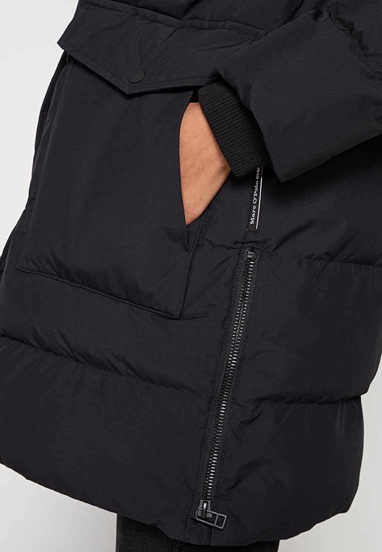 Schwarze Steppjacke mit Reißverschluss, elastischen Bündchen und einer großen Außentasche vorne, gefertigt aus strukturiertem, isolierendem Stoff.