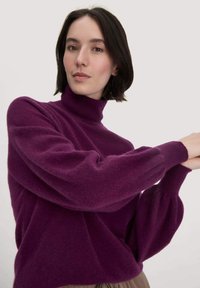 Pflaumenvioletter Rollkragenpullover aus weichem, strukturiertem Stoff; verfügt über Puffärmel und gerippte Bündchen für zusätzliche Details.