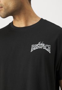 Melna kokvilnas T-kreklā ar baltu izšūtu "Benfica" logotipu uz krūšu, ar apaļu kakla izgriezumu un īsām piedurknēm, ar gludu audumu.