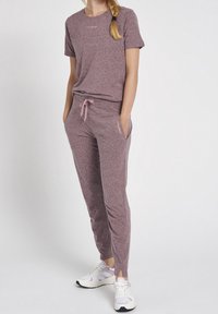 Dwuczęściowy zestaw sportowy w melanżowym kolorze fiołkowym. Koszulka z krótkimi rękawami, a spodnie mają ściągacz w pasie i kieszenie.