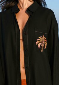 Black button-up shirt made of lightweight fabric, featuring a chest pocket with colorful palm tree embroidery and contrasting pink stitching.