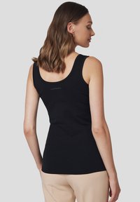 Czarny top na ramiączkach o dopasowanym kroju, szerokich ramiączkach, gładkiej strukturze oraz małym logo z tyłu. W zestawie z jasnymi spodniami.