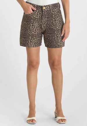 Kort broekje met luipaardprint tot halverwege de dij, gedragen met witte sandalen met hak, voorzien van voorzakken en een gouden knoopsluiting.