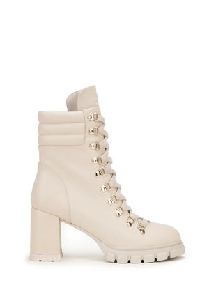 Béžová kožená ankle boot s blokovým podpatkem, se stříbrnými očky na šněrování, polstrovaným límcem a texturovanou podrážkou s drážkami.