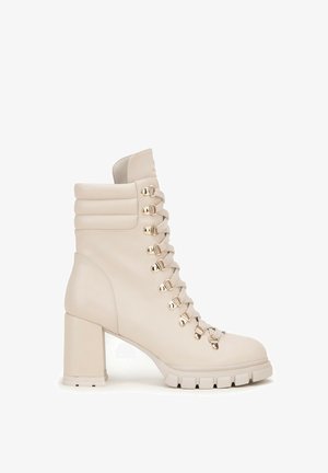 Béžová kožená ankle boot s blokovým podpatkem, se stříbrnými očky na šněrování, polstrovaným límcem a texturovanou podrážkou s drážkami.