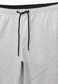 Lys grå sweatpants med en sort snøre i livet, der har en glat tekstur og skrå sidelæg for ekstra detaljer.
