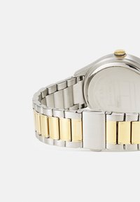 Rustfrit stål ur med et tofarvet armbånd, der har sølv- og guldlænker. Rund urkasse med en gul accent på kronen.