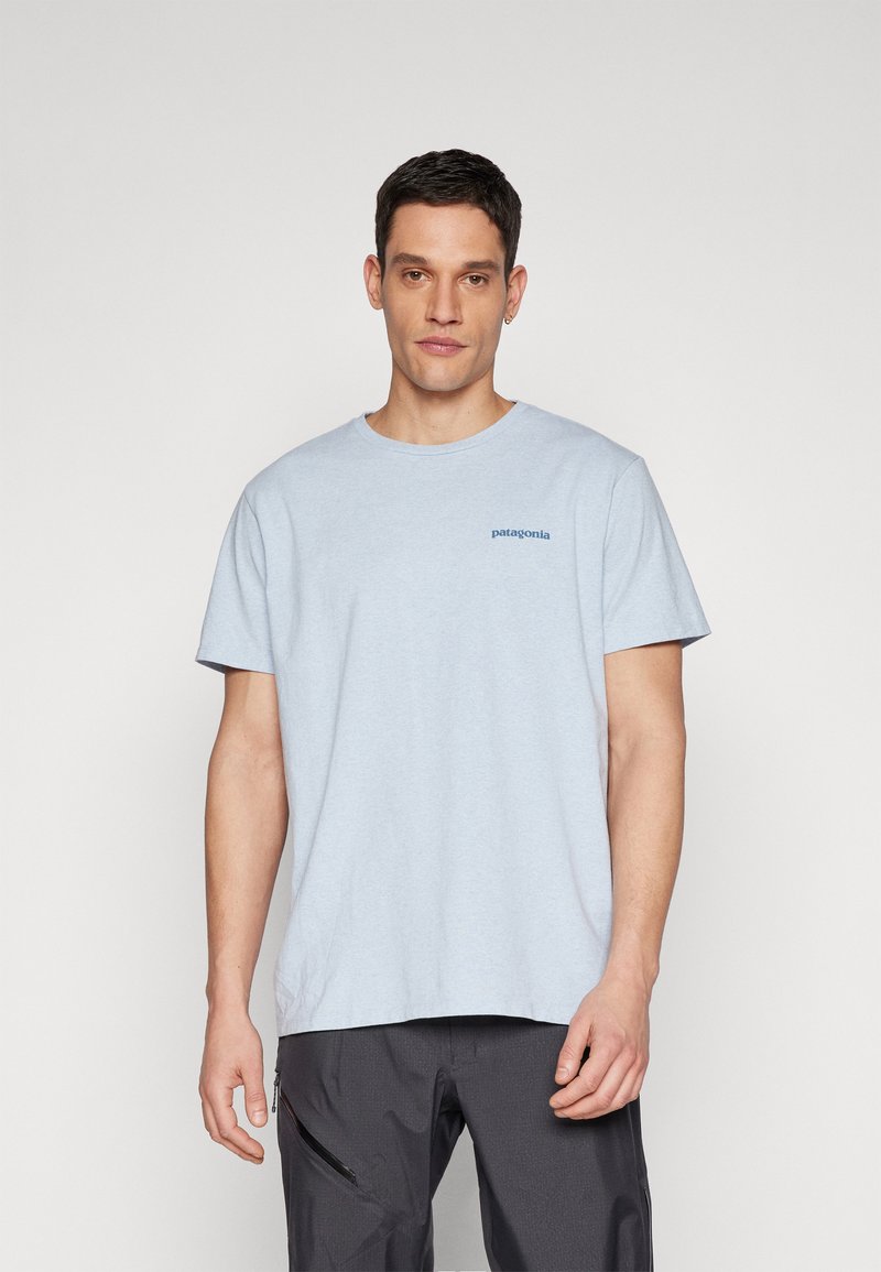 Camiseta de algodón de color azul claro con cuello redondo, que presenta un pequeño logo en azul oscuro de "patagonia" en el lado izquierdo del pecho. Mangas cortas y corte relajado.