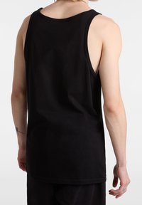 Personne portant un débardeur noir uni sans manches, vue de derrière, avec un petit tatouage sur l'avant-bras gauche et une bague à la main droite.