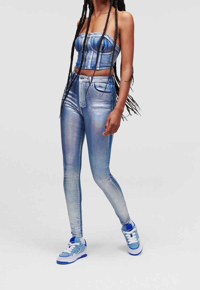 Sininen denimi lyhyt toppi, jossa on rakenteellinen muotoilu ja korkeavyötäröiset, slim fit -farkut. Kankaan pinta on kiiltävä ja hohtava. Siniset tennarit valkoisilla yksityiskohdilla.